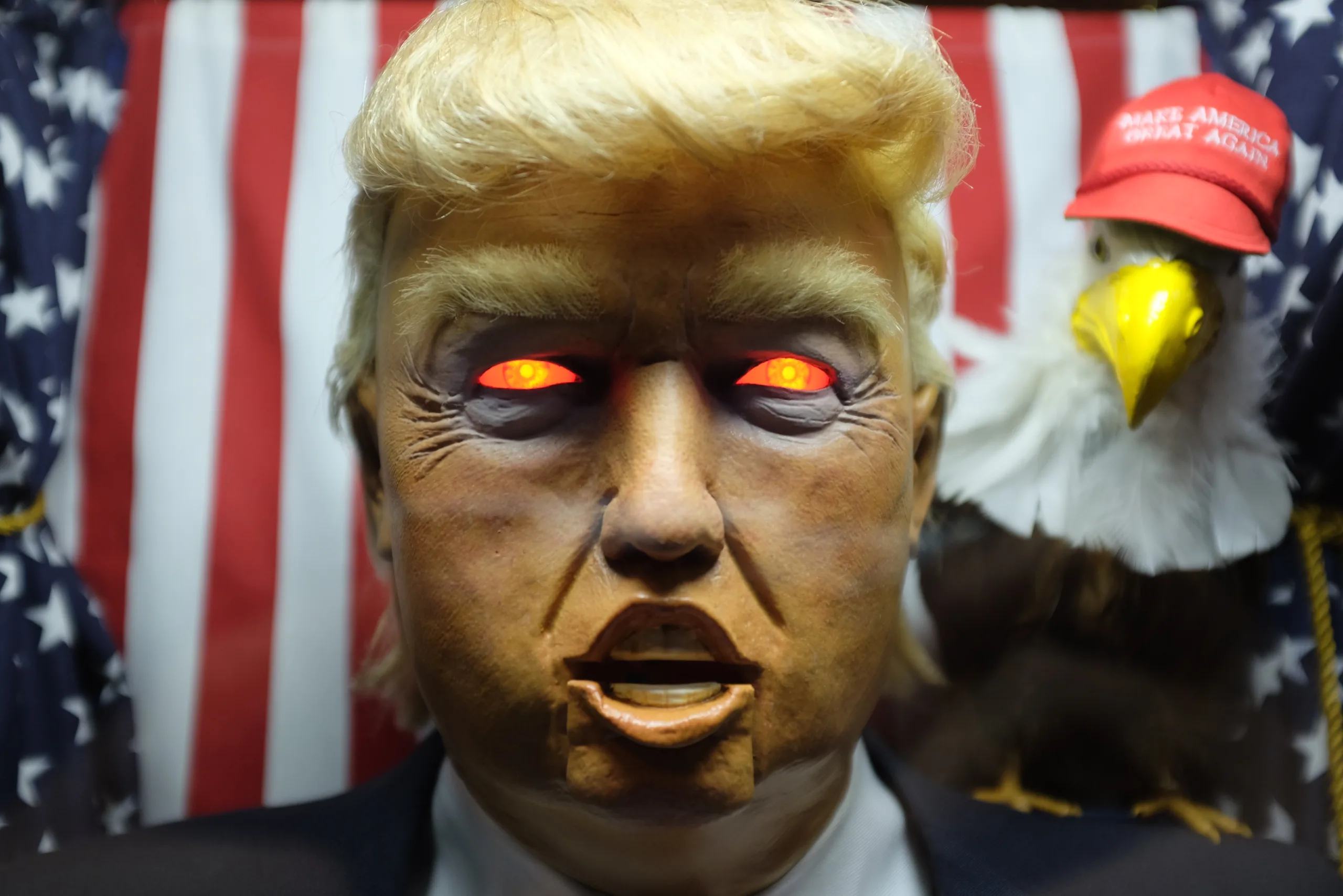 The All Seeing Trump machine: animatronic Trump with glowing red eyes, eagle in a MAGA hat behind